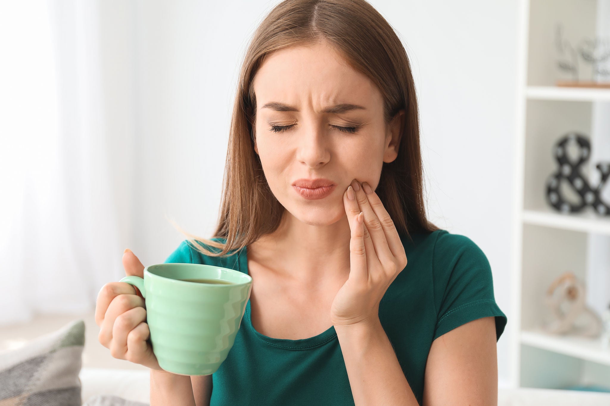 Young woman with sensitive teeth and cup of hot coffee at home